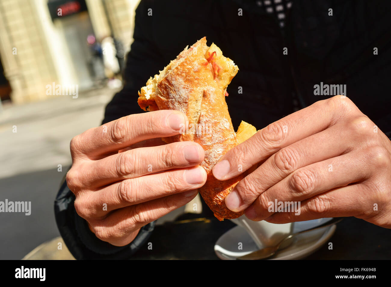 young man sitting in a table in the terrace of a cafe eating a spanish omelette sandwich Stock Photo