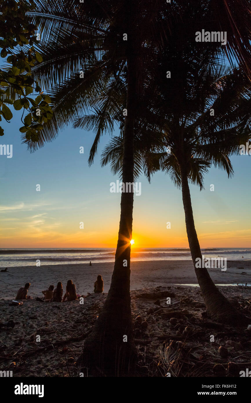 People by palm trees at sunset on Playa Hermosa beach, far south of the Nicoya Peninsula, Santa Teresa, Puntarenas, Costa Rica Stock Photo