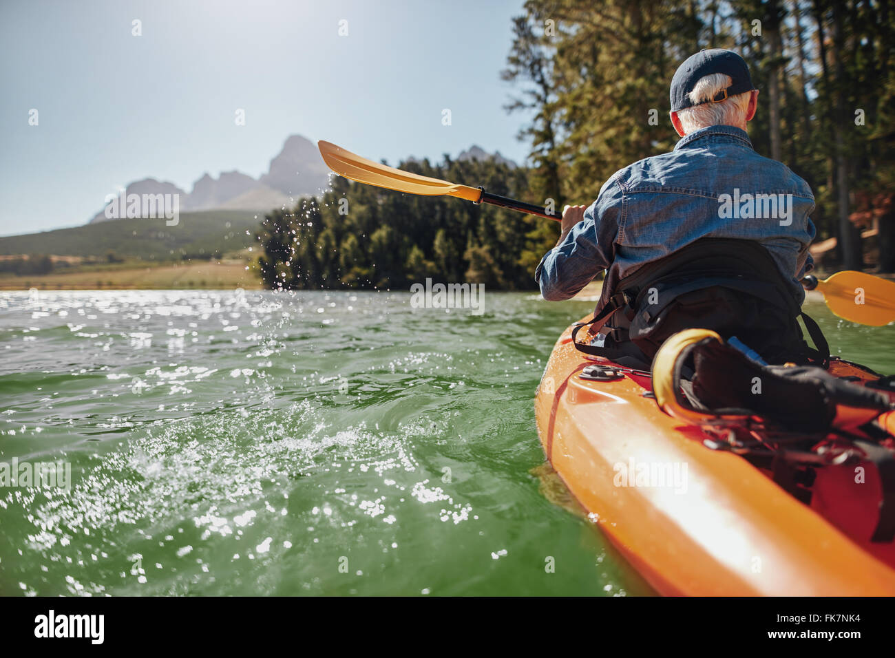 Rear view image of a man canoeing in a lake. Man paddling a kayak on summer day. Stock Photo