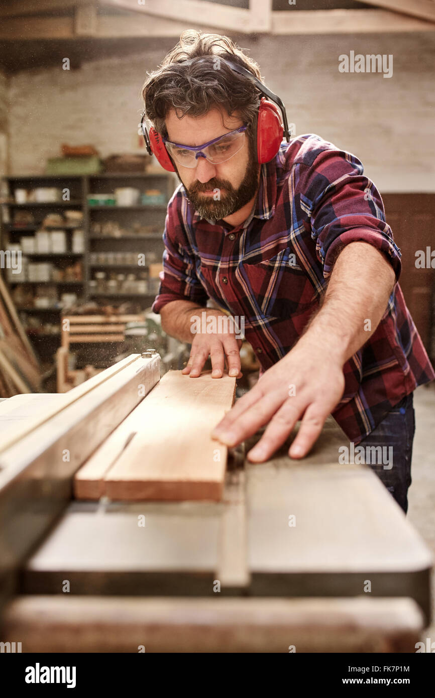 Carpenter wearing protective gear cutting a plank of wood Stock Photo