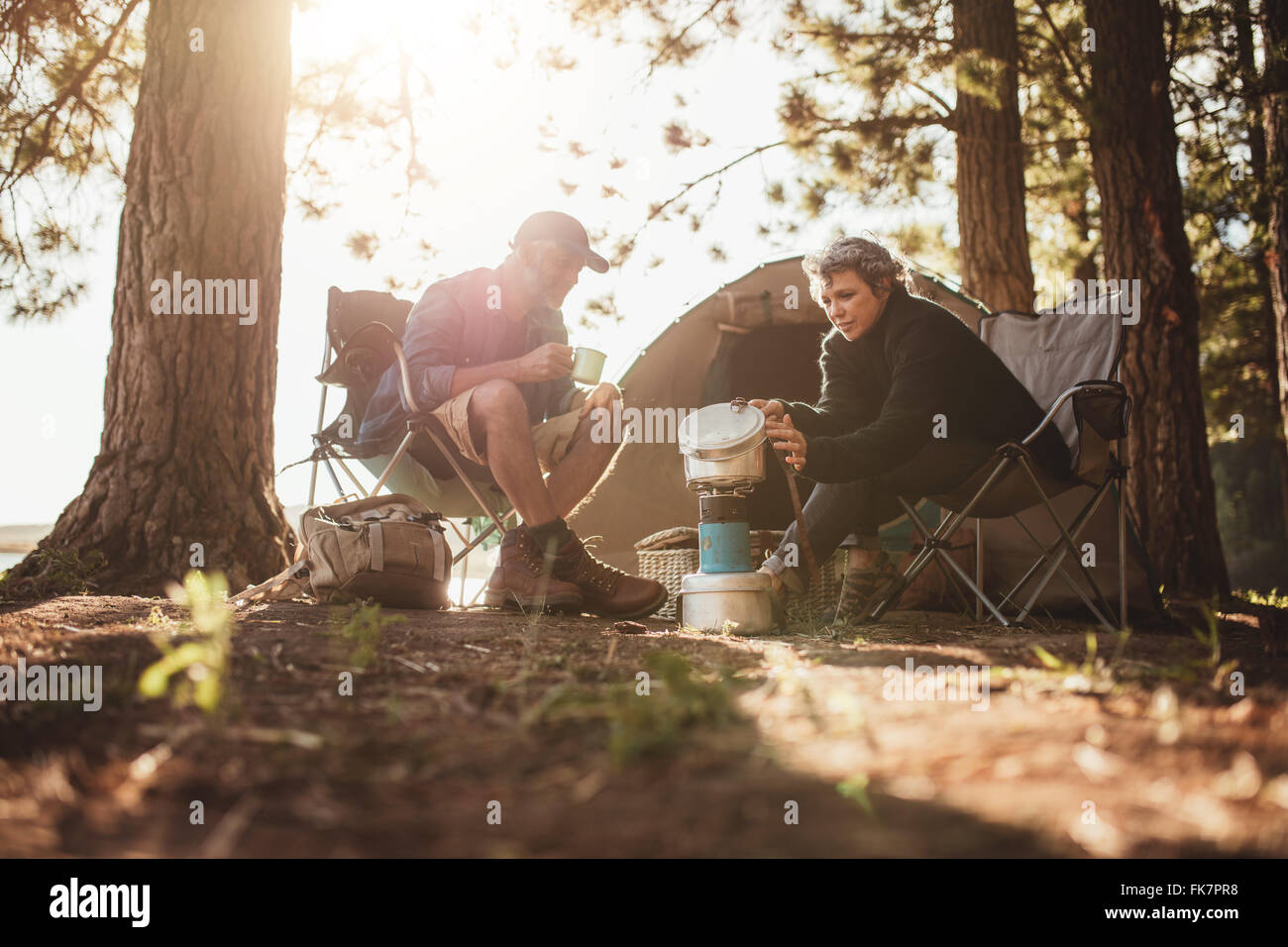 Senior couple cooking and making food outdoors on a camping trip. Mature man and woman sitting outside the tent on a summer day Stock Photo