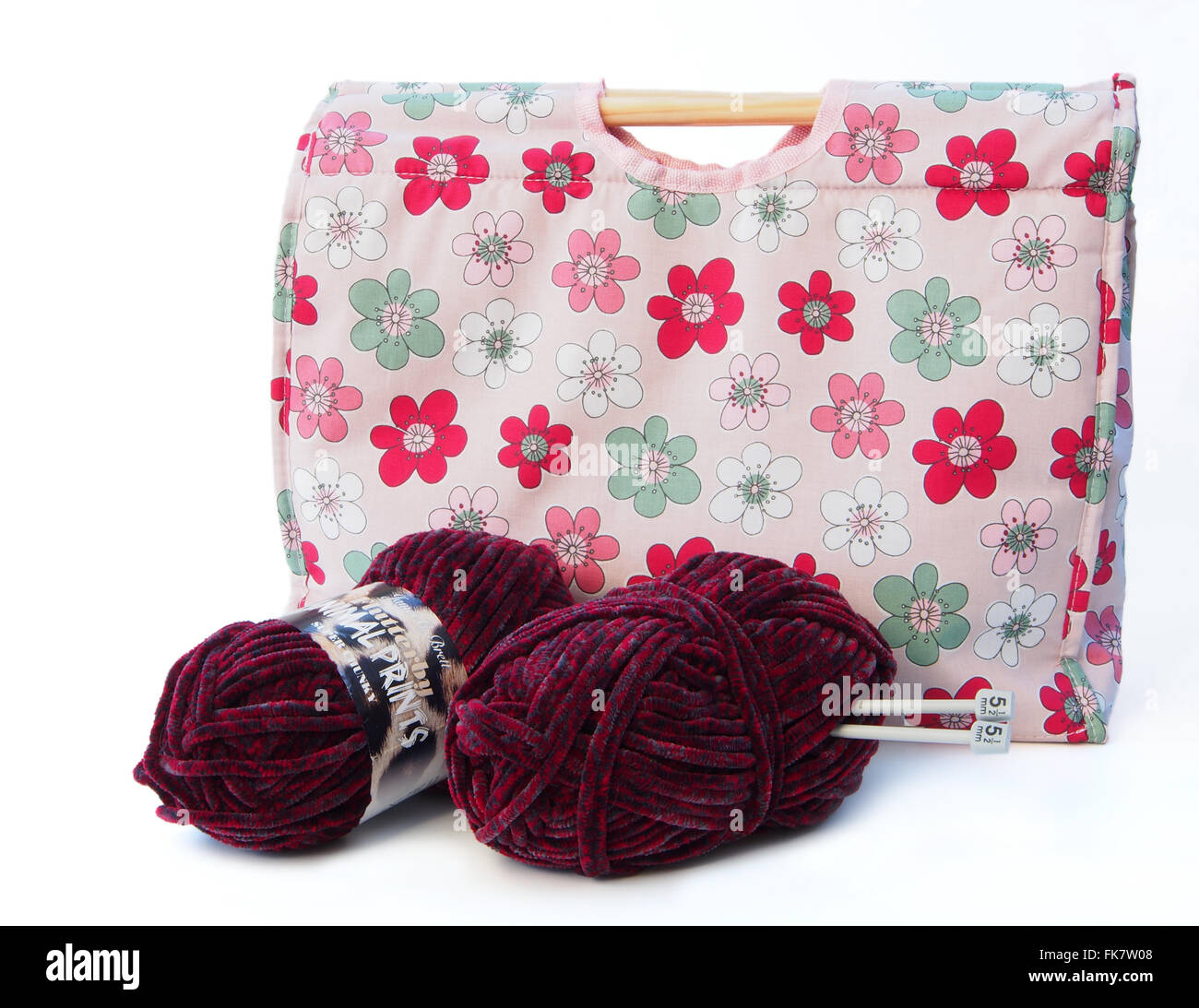 Pink flower patterned knitting / craft bag with knitting needles, and two balls of burgundy coloured wool on a white background. Stock Photo