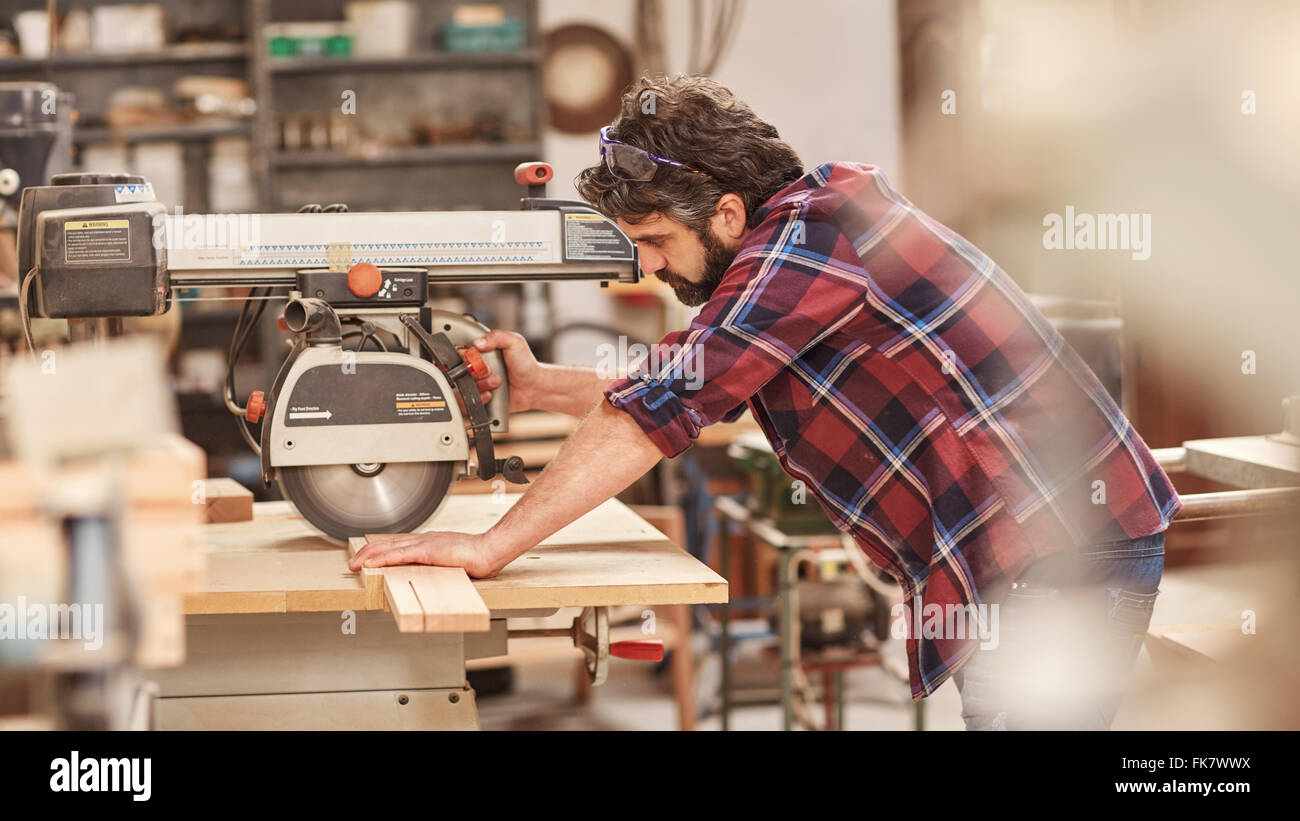Craftsman using radial arm saw on some wood in workshop Stock