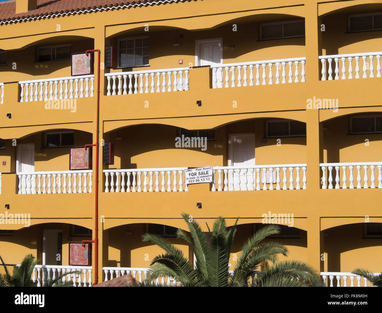 Yellow and white apartment block in Los Gigantes, Tenerife Spain, with for sale sign in English on the balcony Stock Photo