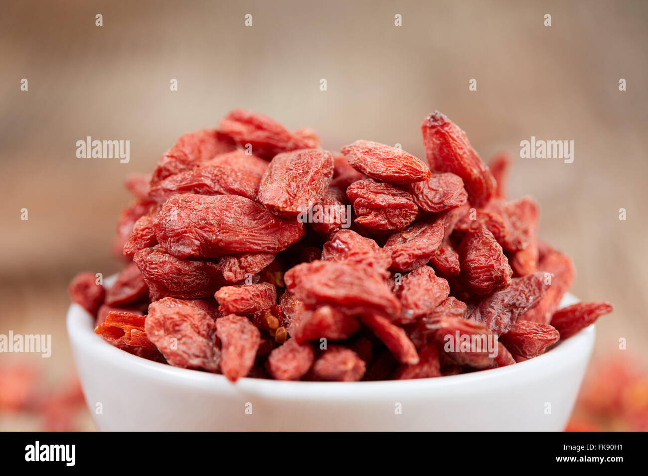Goji berries super food with antioxidants, minerals and vitamins in a white china bowl on a brown wooden table Stock Photo