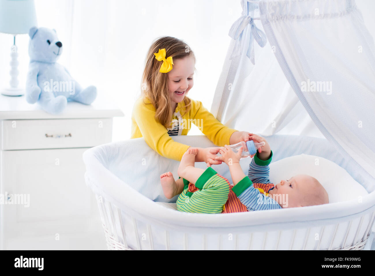 Little girl giving baby brother bottle with water or milk. Healthy