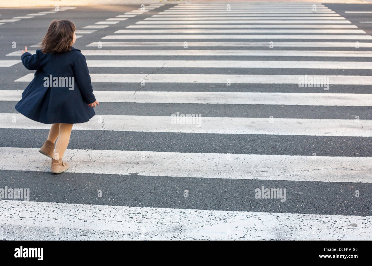 Little girl running and crossing alone a crosswalk. Dangerous behavior Stock Photo