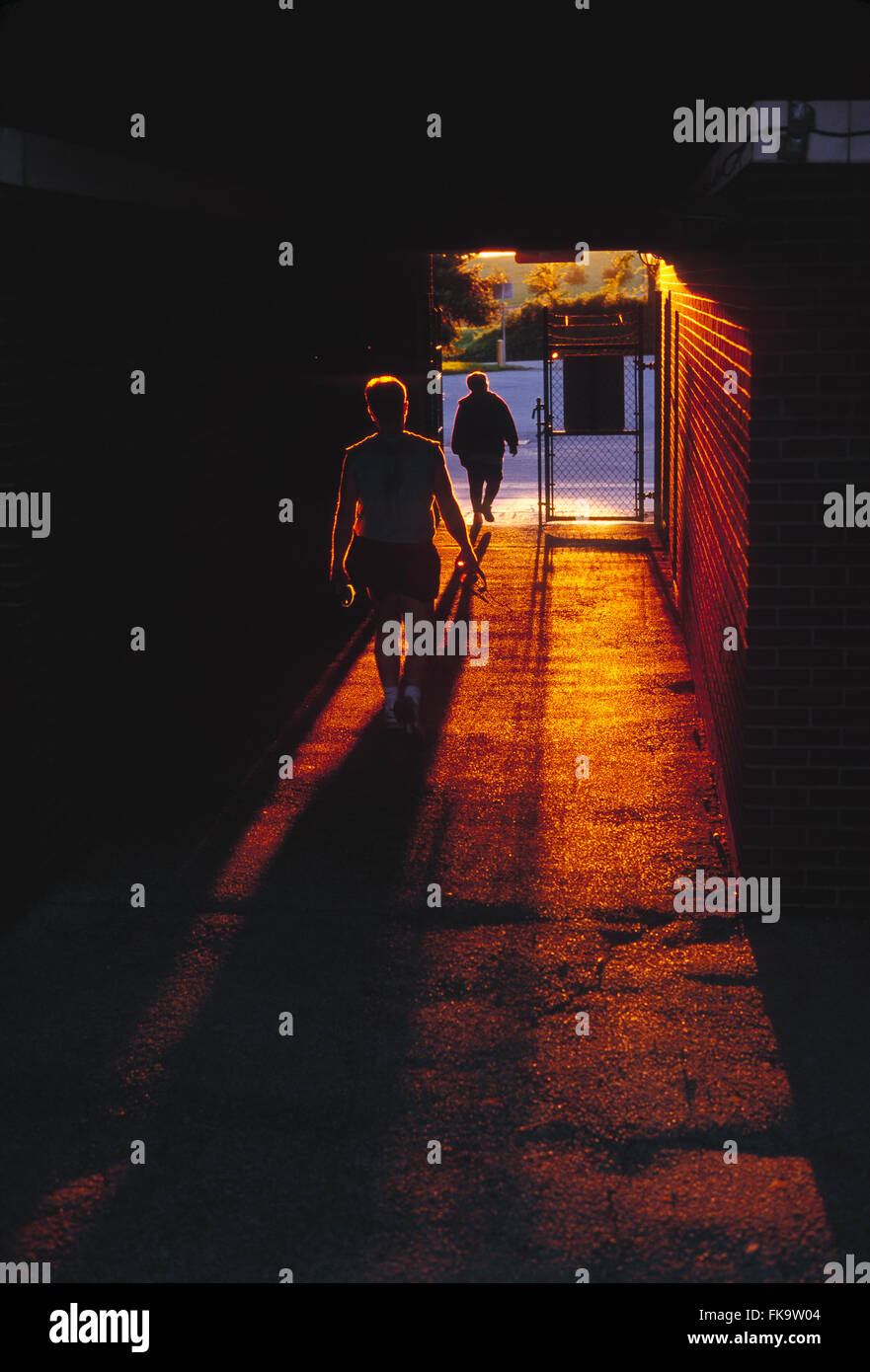 Sunset illuminates male runners leaving stadium track through tunnel Stock Photo