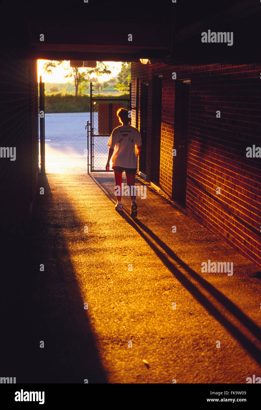 Sunset illuminates female runner leaving stadium track through tunnel Stock Photo