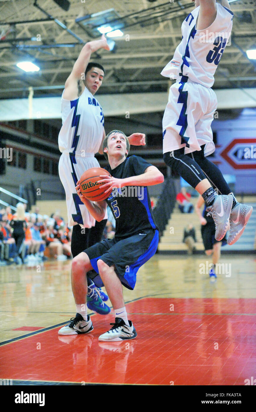 In the apparent court of giants a high school guard waits for the high-flying traffic of two defenders to clear before shooting. USA. Stock Photo