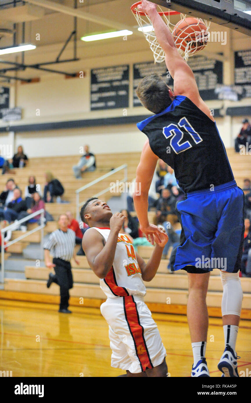 A high school center in the process of slam dunking the basketball above an onlooking opponent during a tournament game. USA. Stock Photo