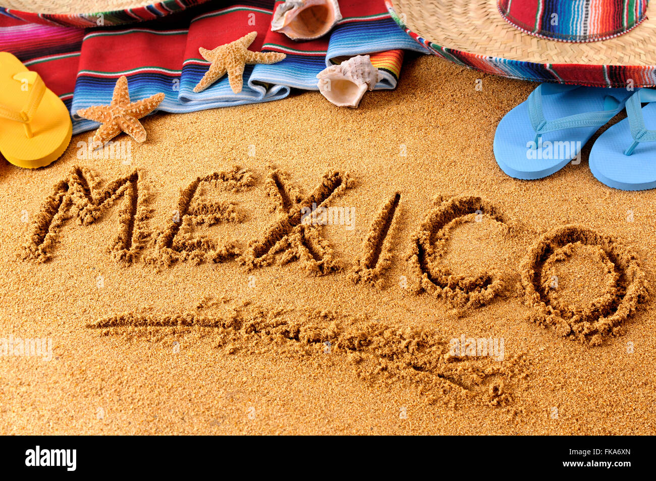 The word Mexico written in sand on a Mexican beach, with sombrero, straw hat, traditional serape