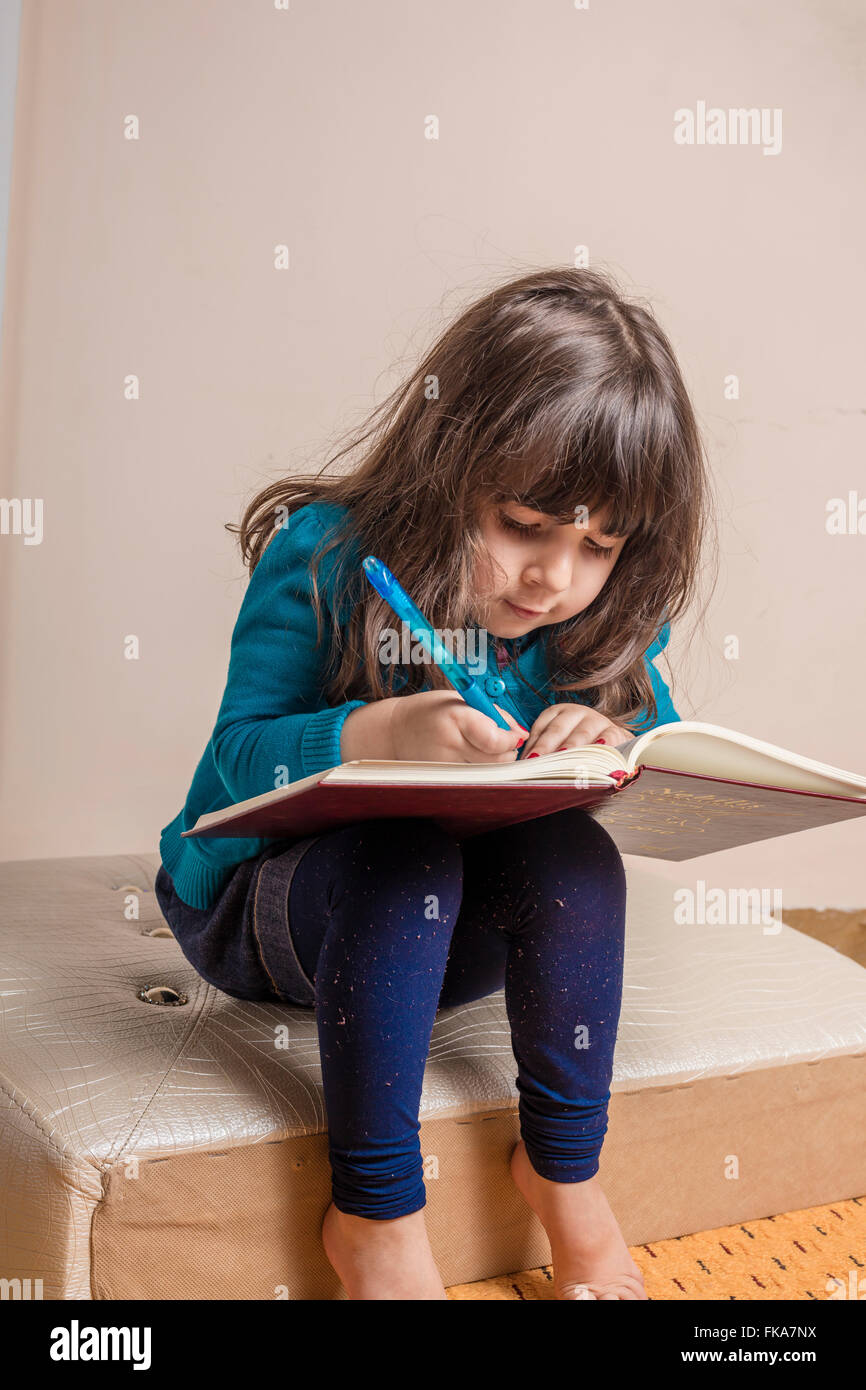 Samll girl inside studio with red copybook and blue pen in hand in hand Stock Photo
