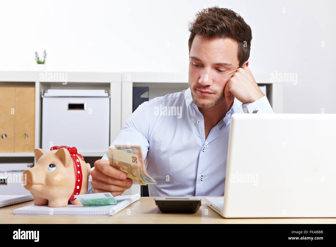 Worried business man with money and piggy bank in office Stock Photo
