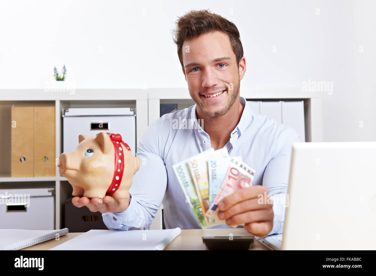 Happy business man with piggy bank and money in office Stock Photo - Alamy