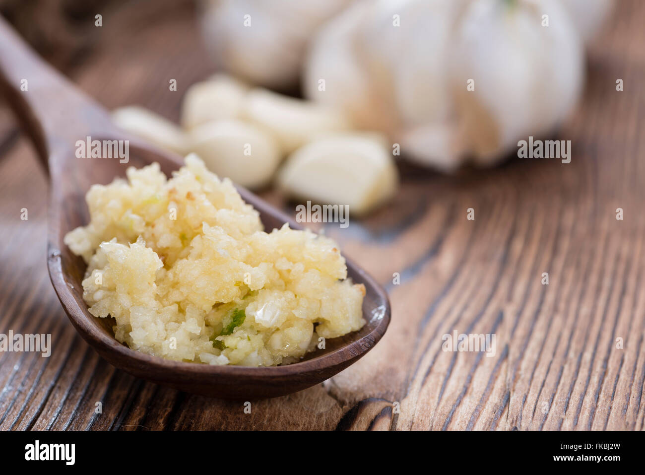 Crushed Garlic (closeup shot) on rustic wooden background Stock Photo