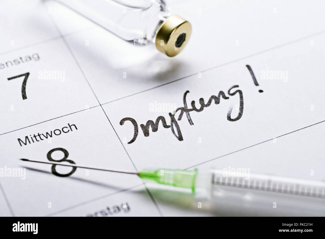 appointment book with the word "Impfung" for vaccination, a syringe and a vial of vaccine. Stock Photo