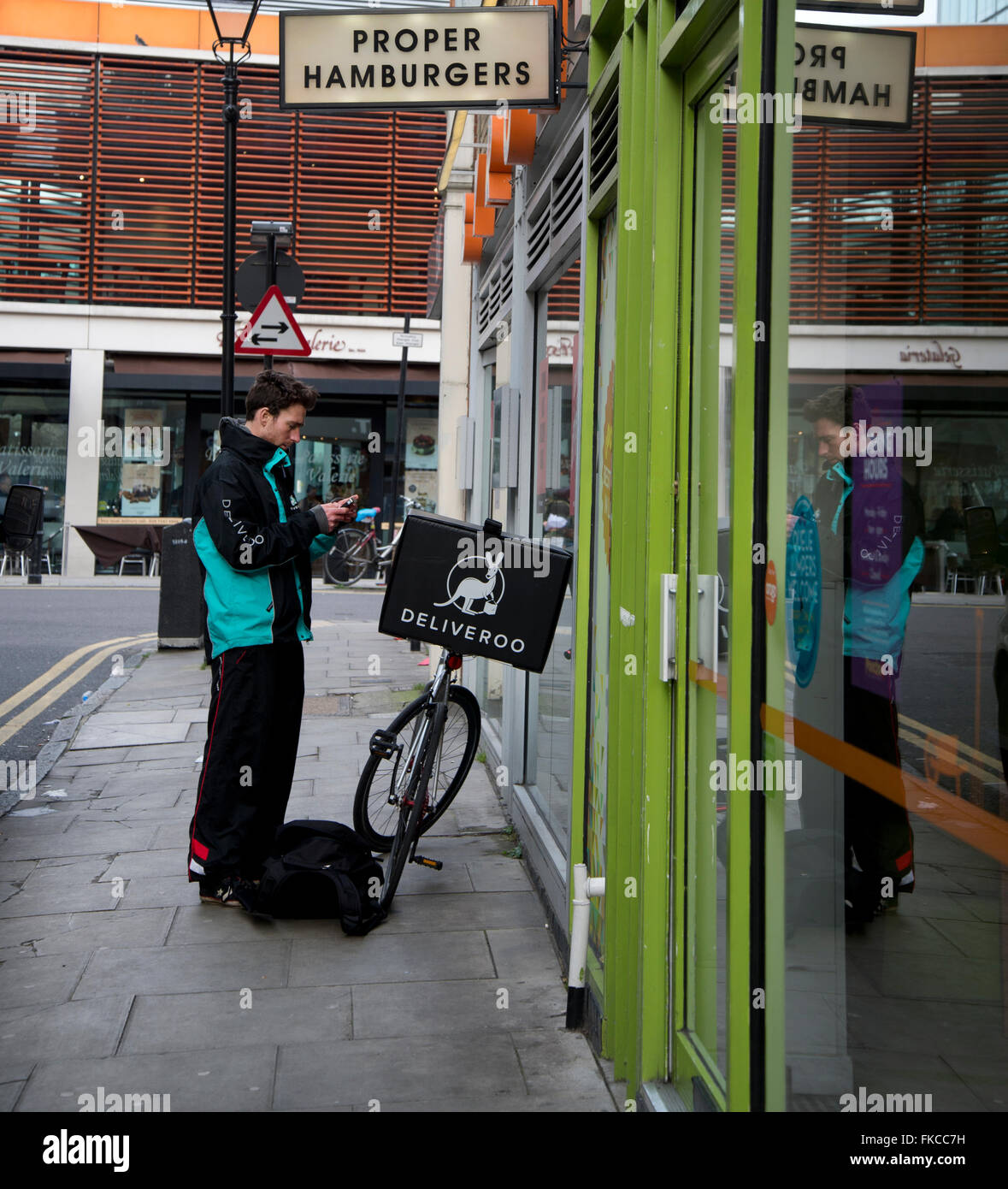 London. Spitafields, Shoreditch. A Deliveroo (food delivery) worker checks his mobile phone. Stock Photo
