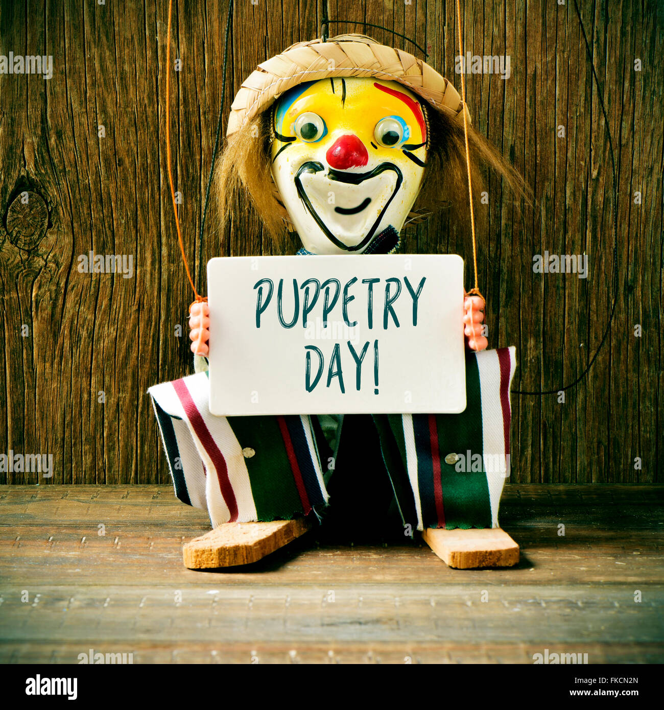 closeup of an old marionette with its face painted as a clown holding a signboard with the text puppetry day Stock Photo