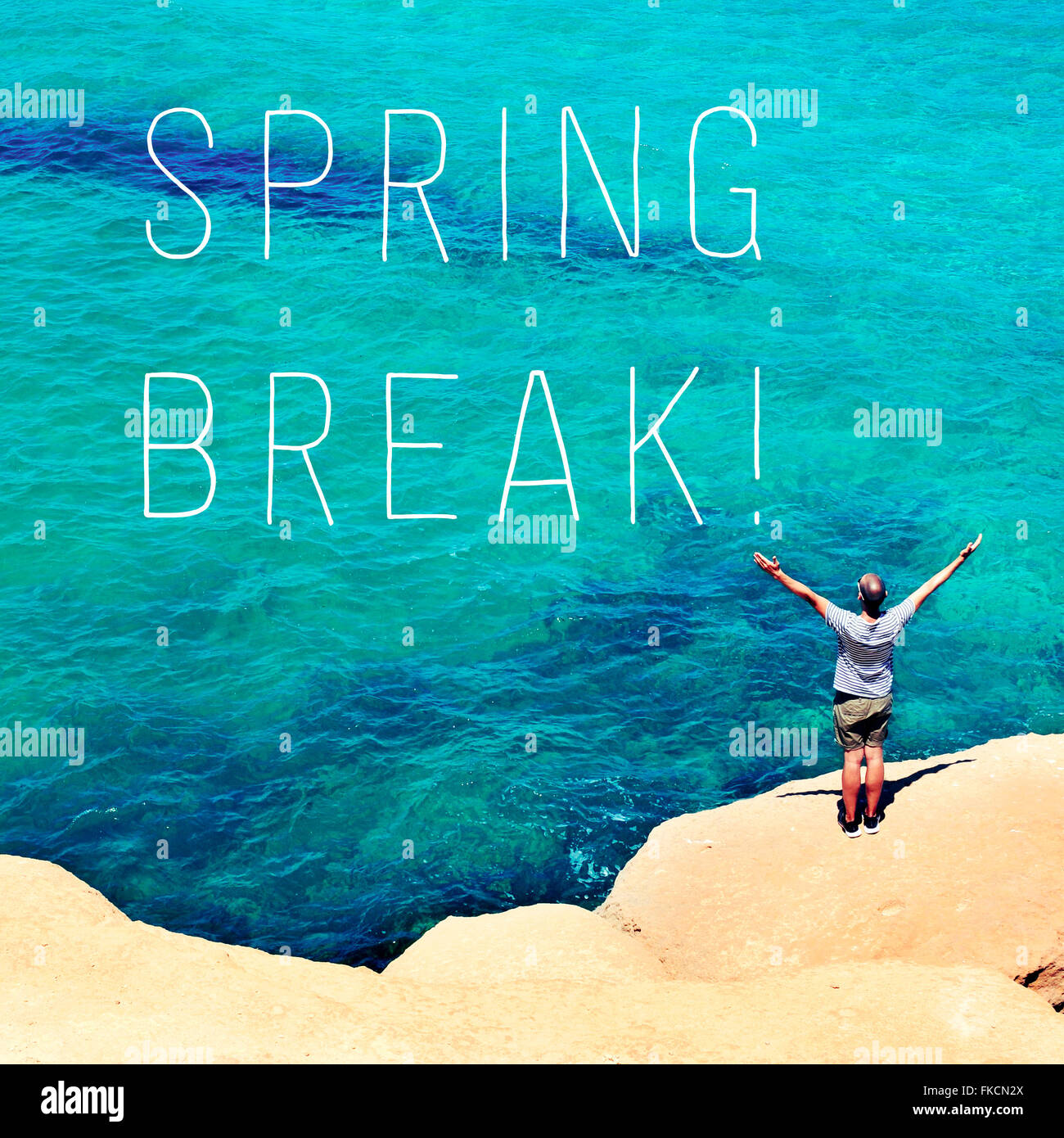 a young man seen from behind with his arms in the air in front of the ocean and the text spring break Stock Photo