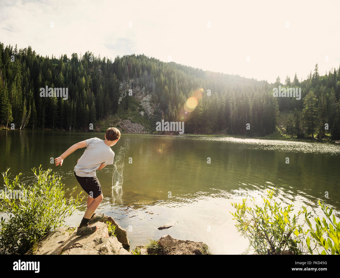 Boy (12-13) throwing stone into lake Stock Photo