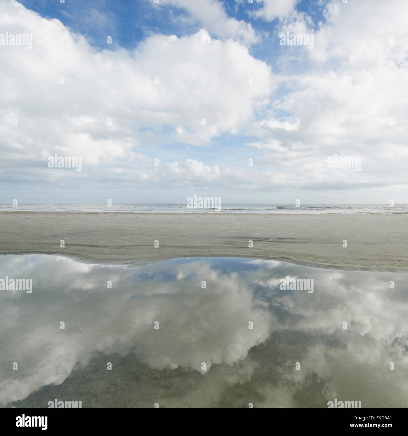 Reflection of clouds in puddle, sea in background Stock Photo