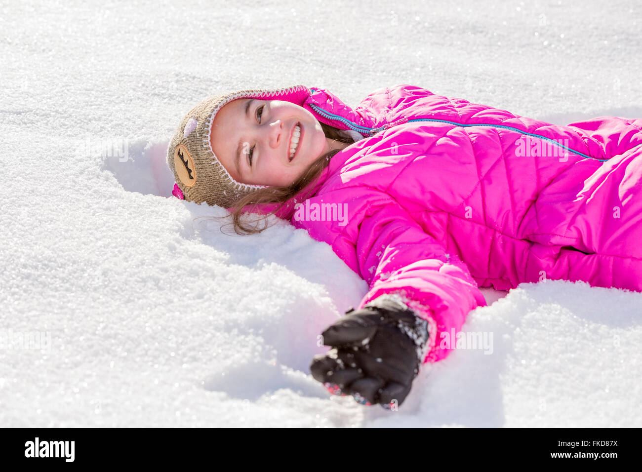 Girl (10-11) in pink jacket lying in snow Stock Photo