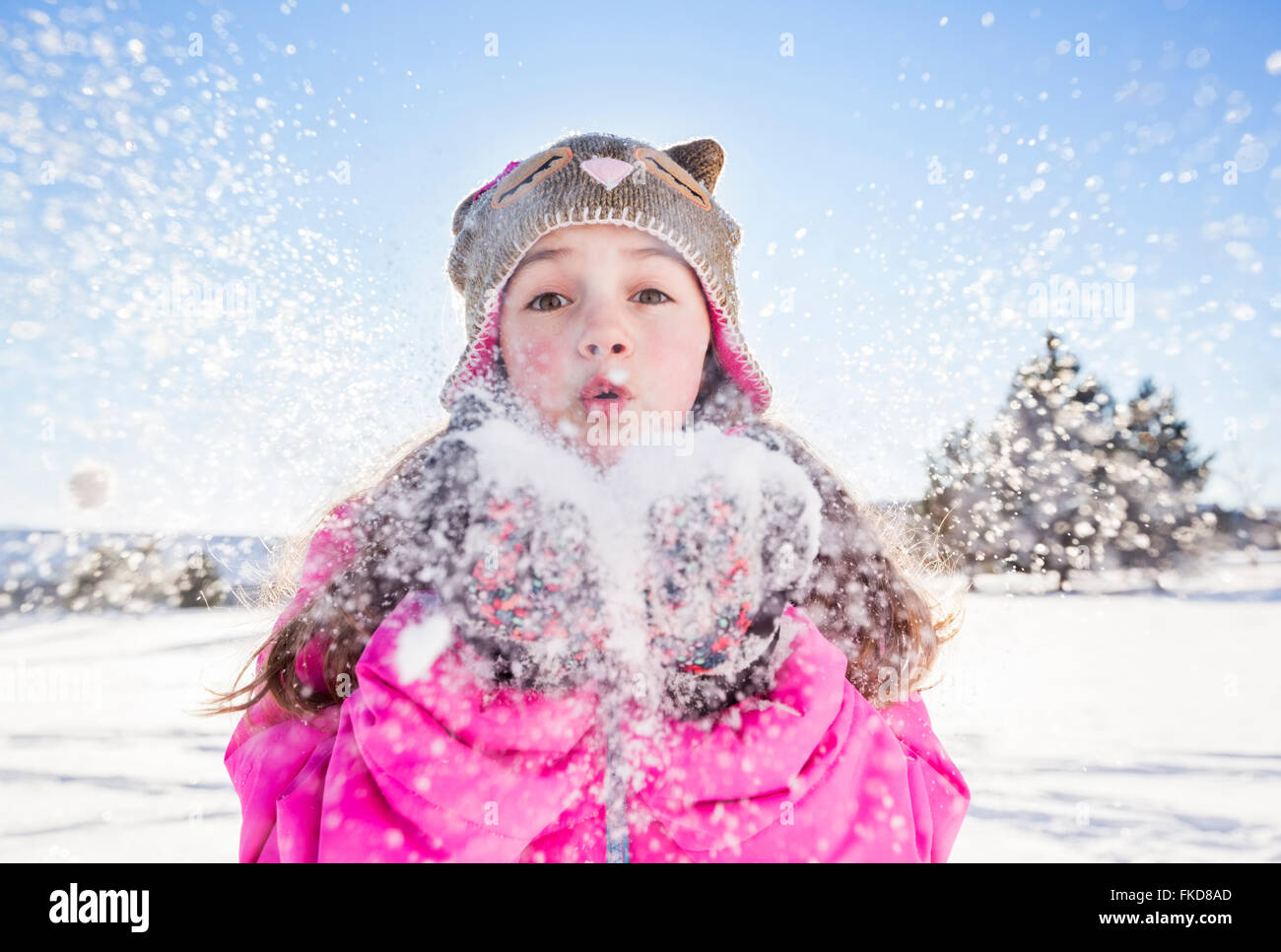 Girl (10-11) in pink jacket blowing snow Stock Photo