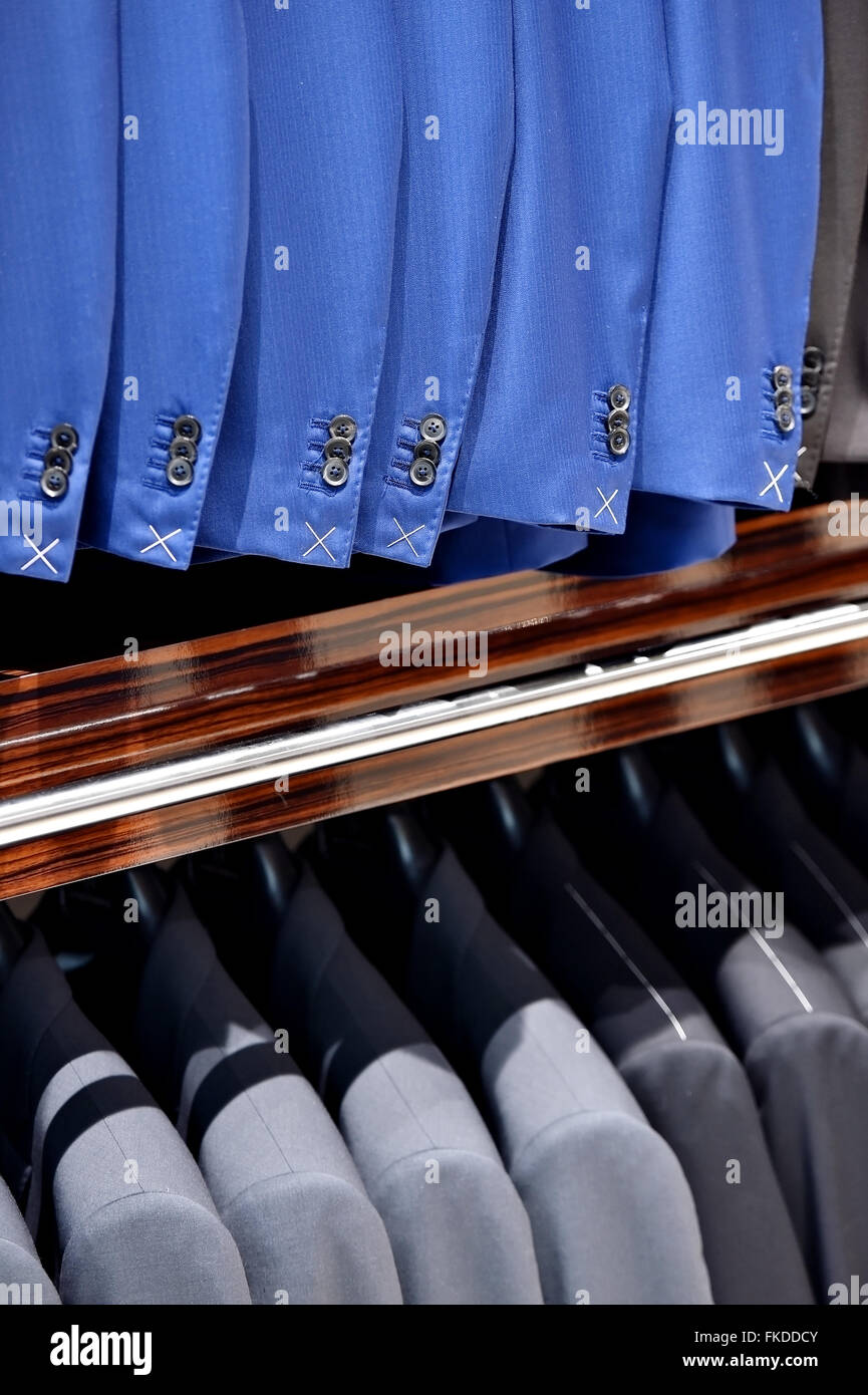 Elegant blue and gray suits on hangers are seen in a suit store Stock Photo