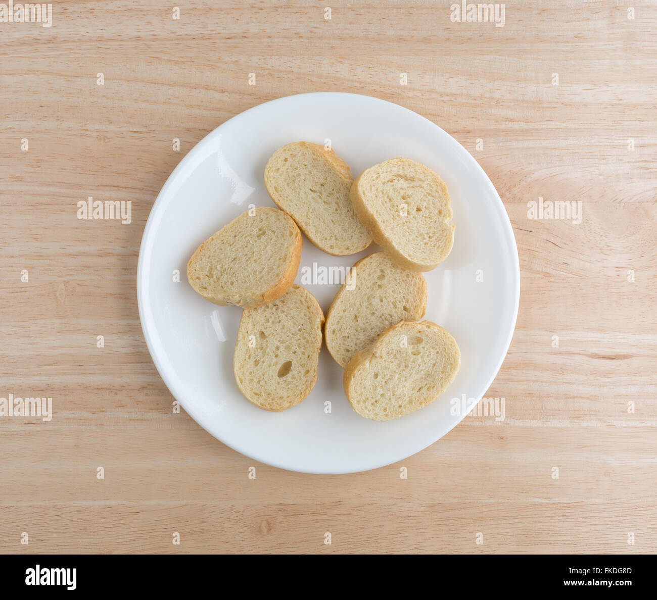 Top view of French bread slices on a white plate atop a wood table top ...