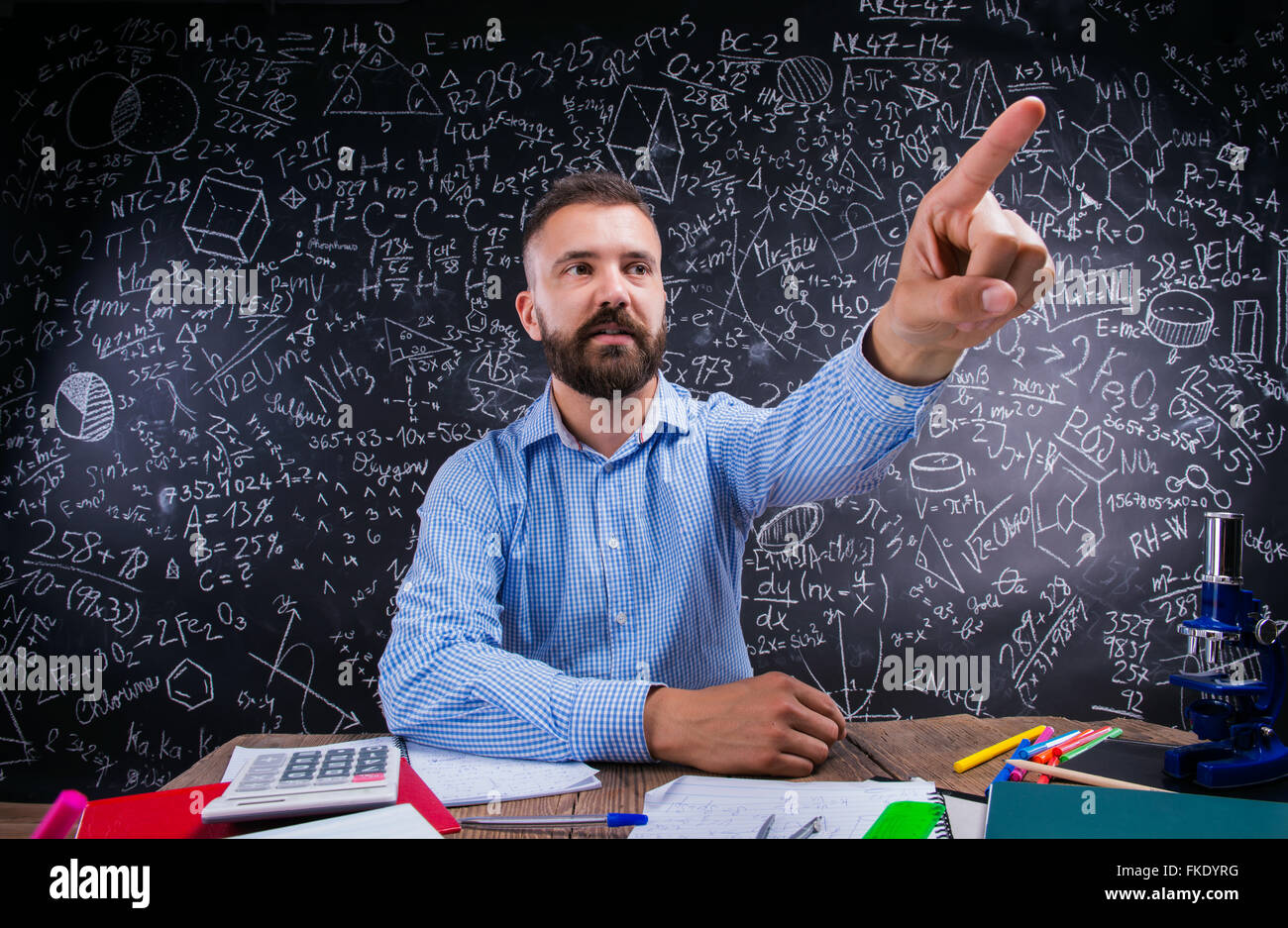 Teacher at desk, school supplies, raised finger, big blackboard Stock Photo