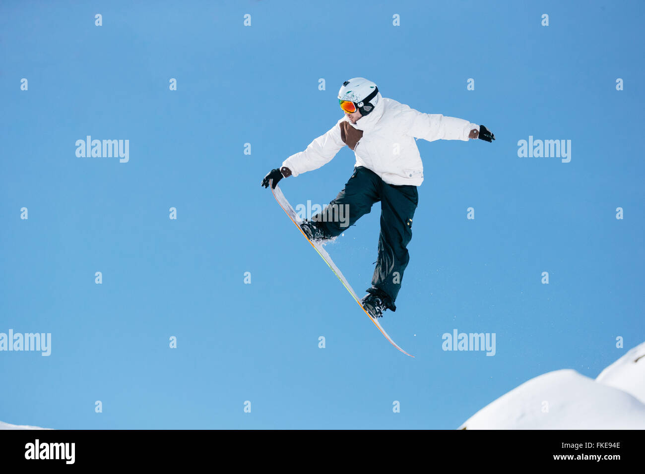 A snowboarder flies through the air against clear blue sky. Stock Photo