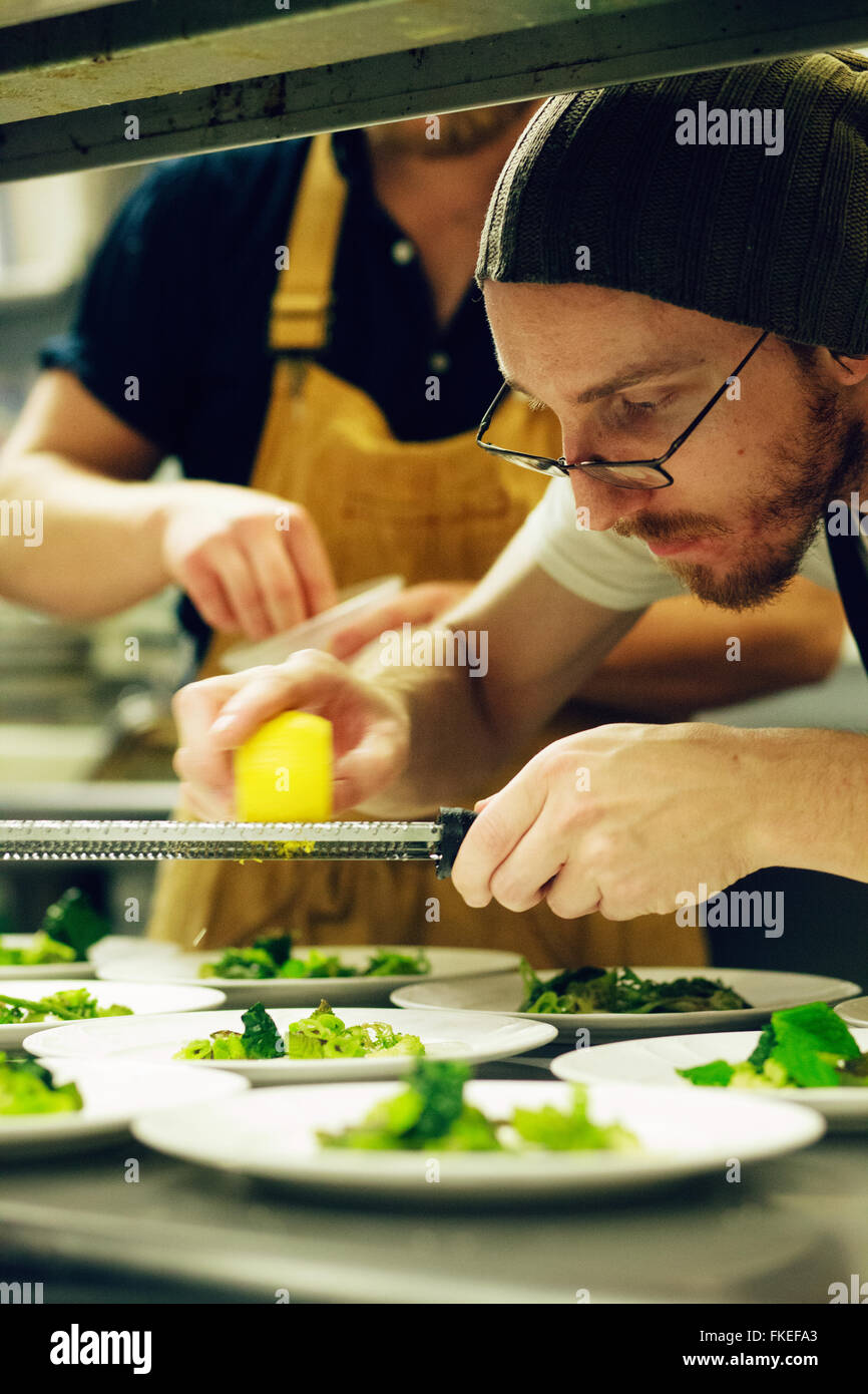 Chef grating cheese over salad in a restaurant kitchen Stock Photo