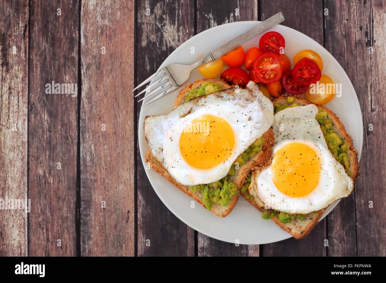 Healthy avocado, egg open sandwiches on a plate with colorful tomatoes against a rustic wood background Stock Photo