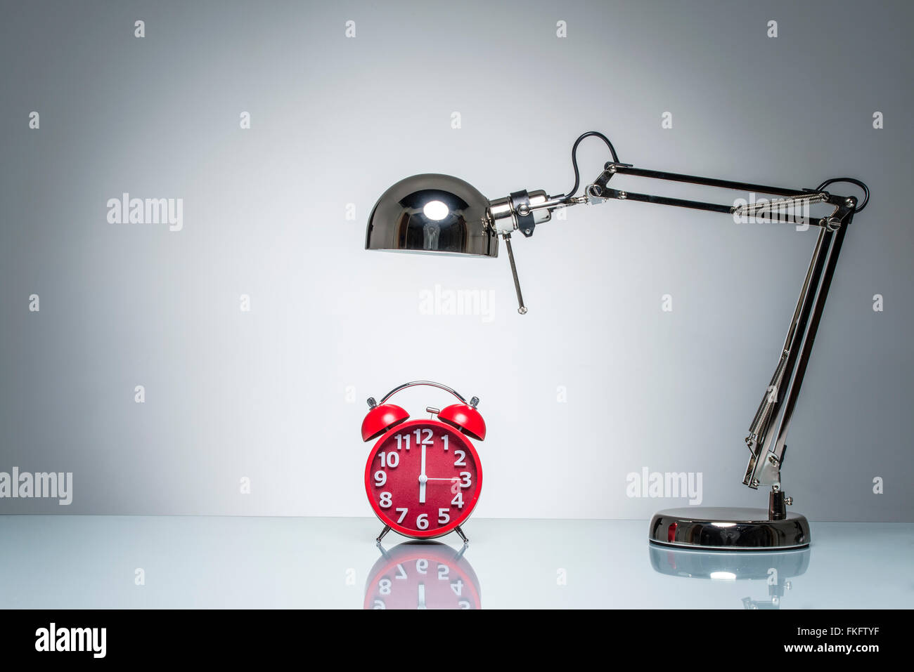 lighting up red alarm clock with desk lamp on round studio lighting Stock Photo