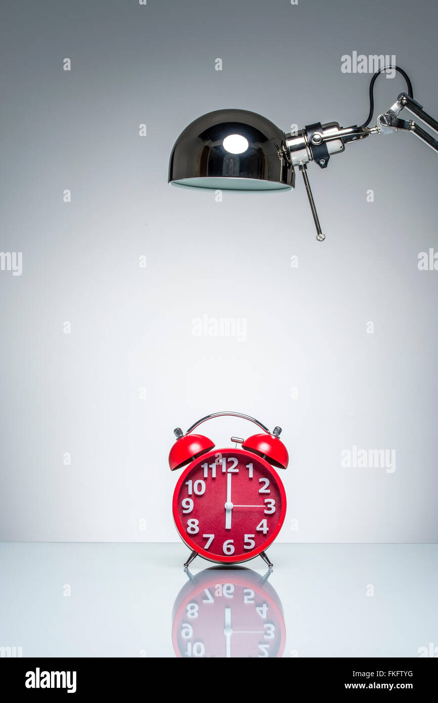 lighting up red alarm clock with desk lamp on round studio lighting Stock Photo