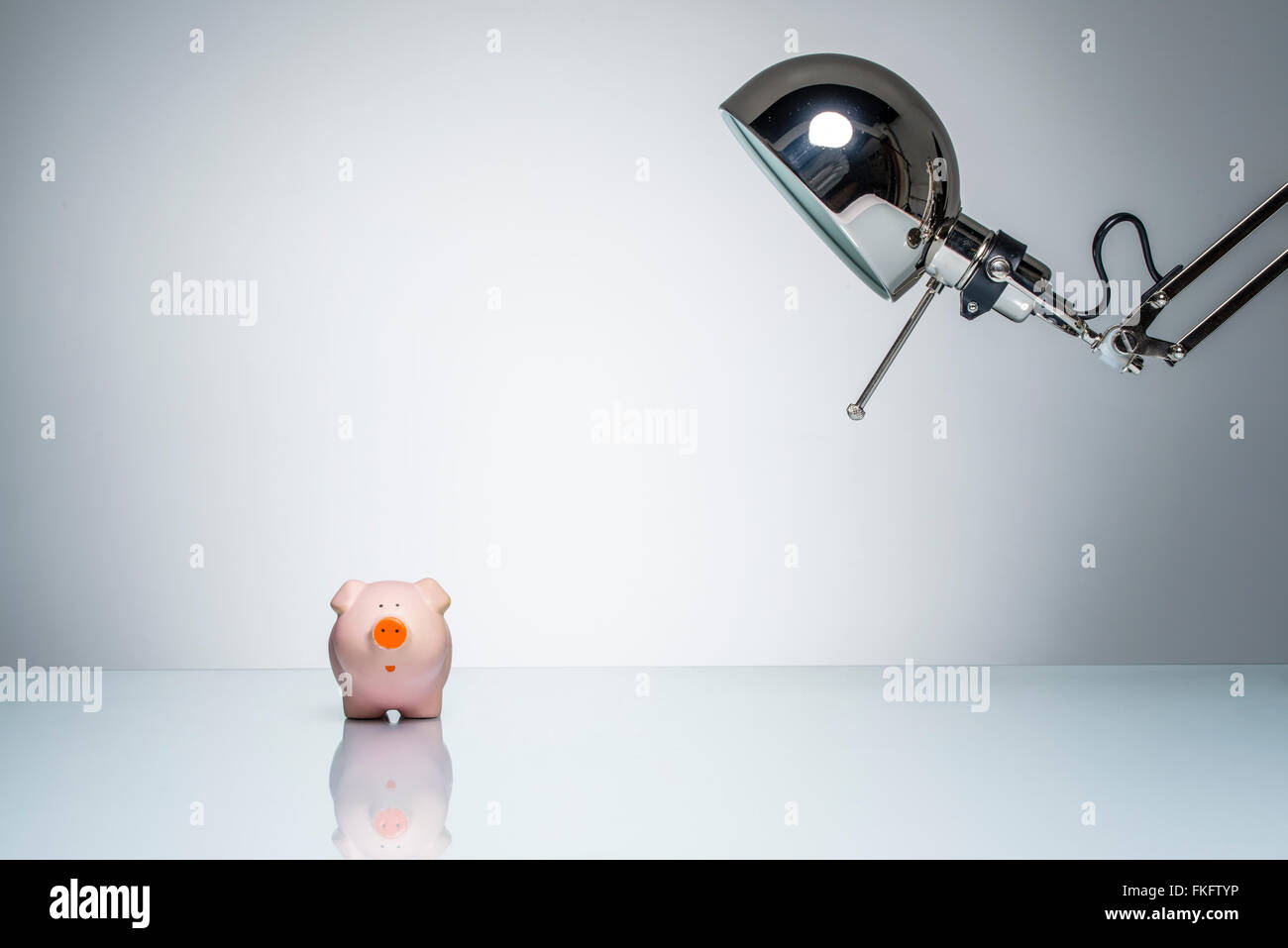 lighting up pink piggy bank with desk lamp on round studio lighting Stock Photo