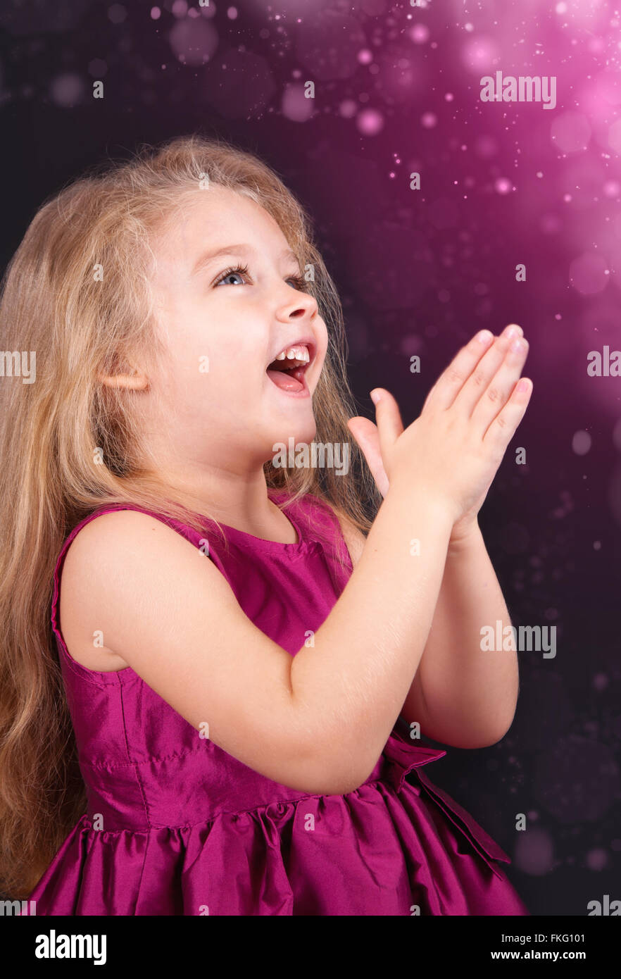 Portrait of a joyful little girl in a pink dress on a black background ...