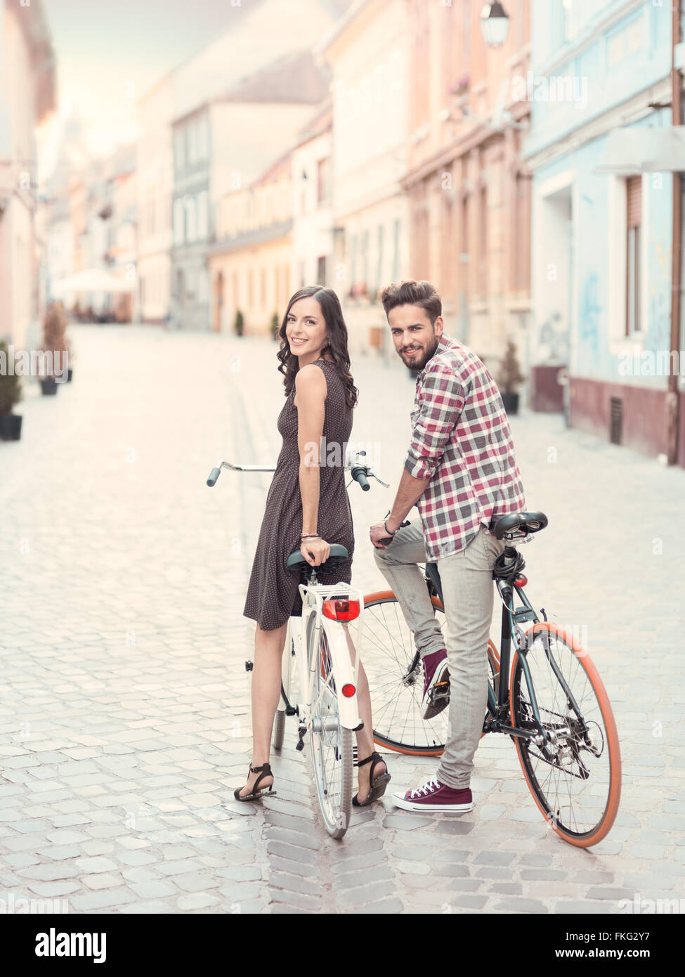 nice young couple , bike stops to turn heads and give a toothy smile toward the camera in a European city in a summer sunny day Stock Photo