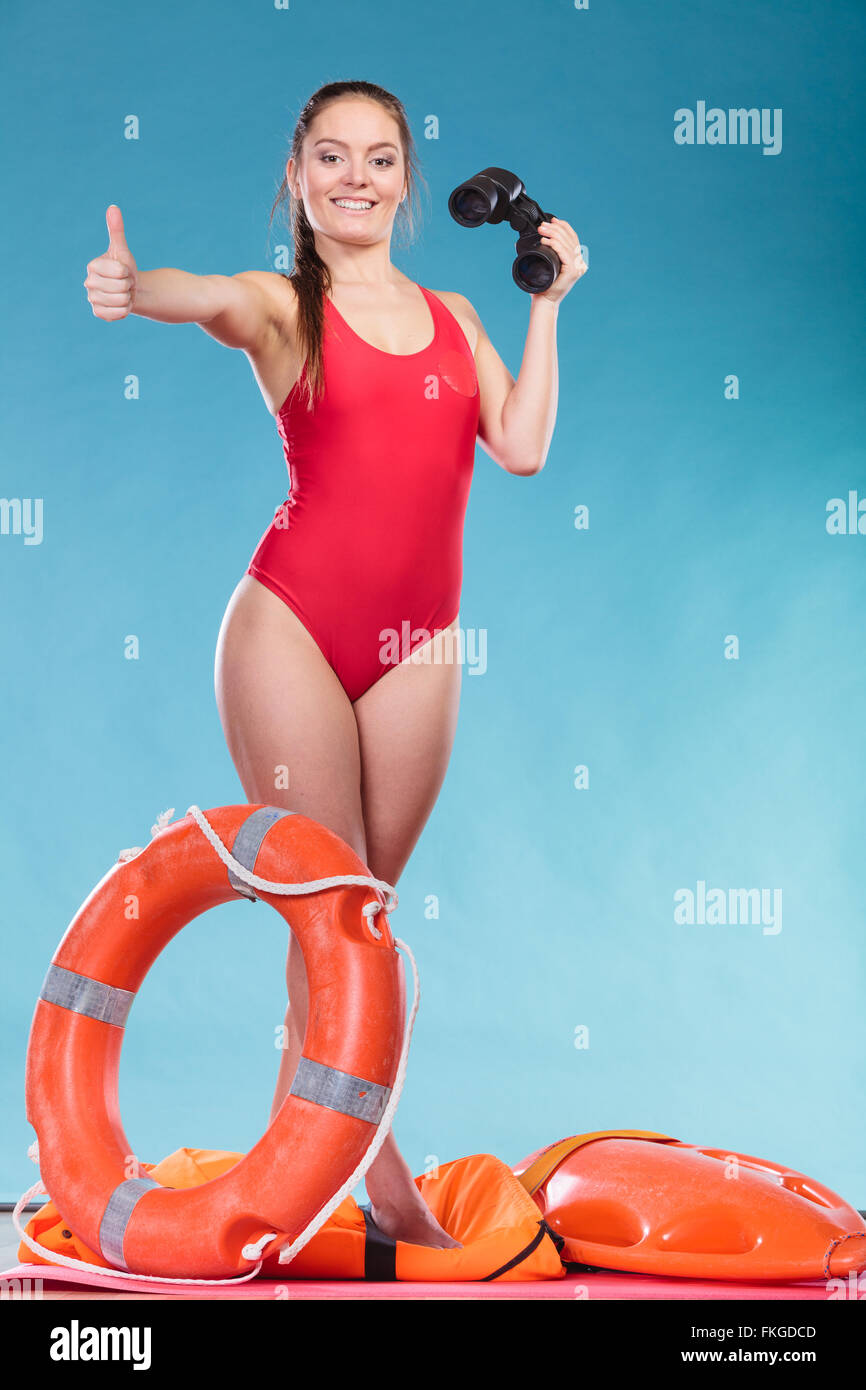 Happy lifeguard with ring buoy lifebuoy and binoculars. Woman girl supervising swimming pool water on blue. Accident prevention. Stock Photo