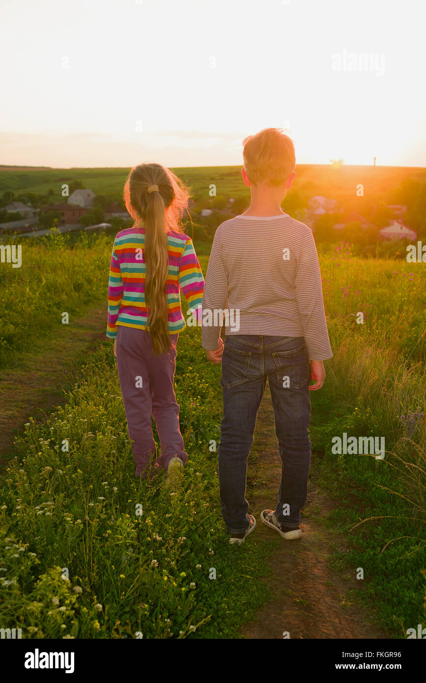 Boy and girl holding hands and walking along the road at sunset ...