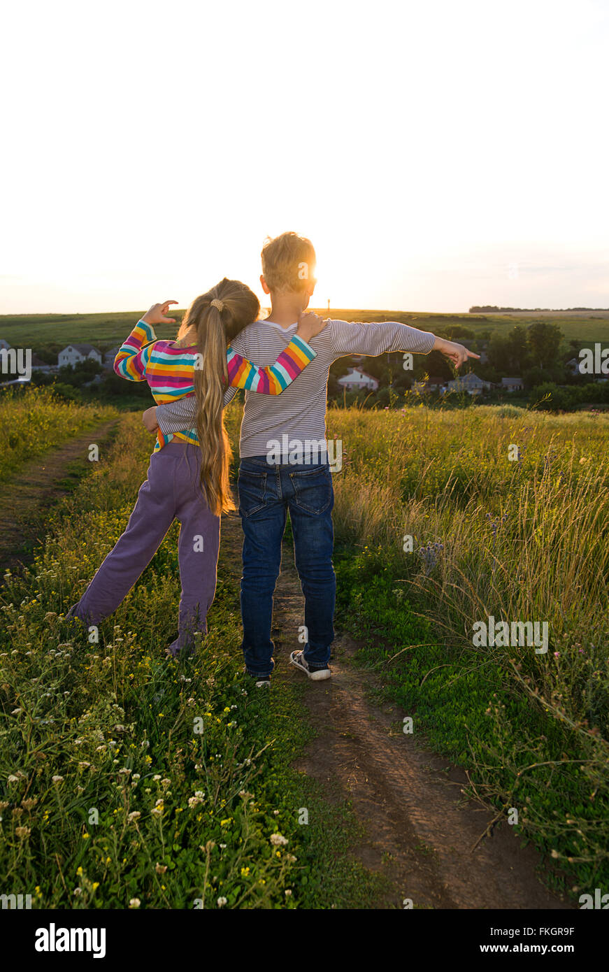 Boy and girl holding hands and walking along the road at sunset Stock Photo