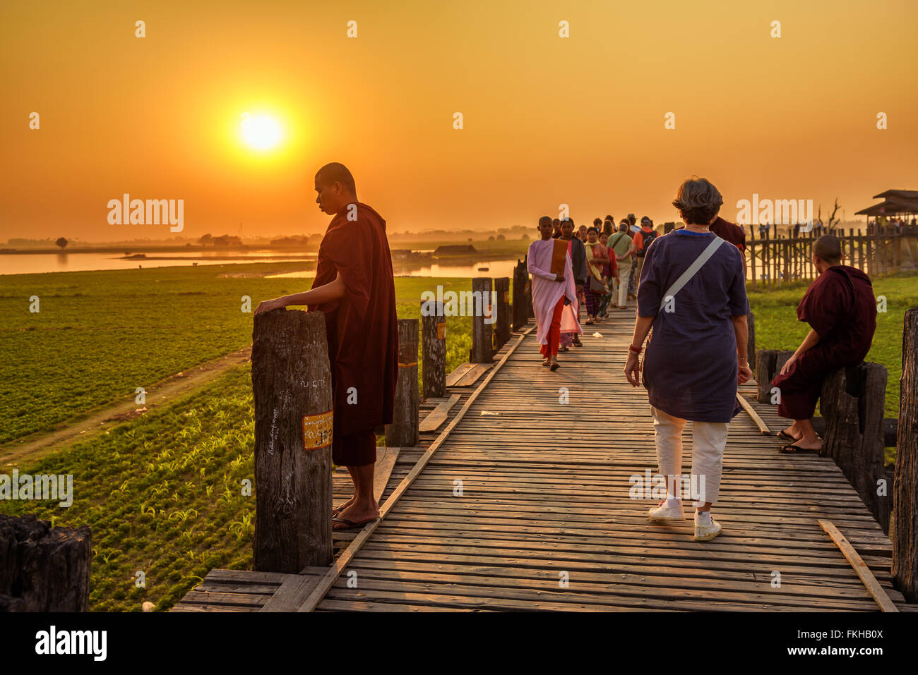 People walking on the historic wooden U Bein Bridge at sunset Stock Photo