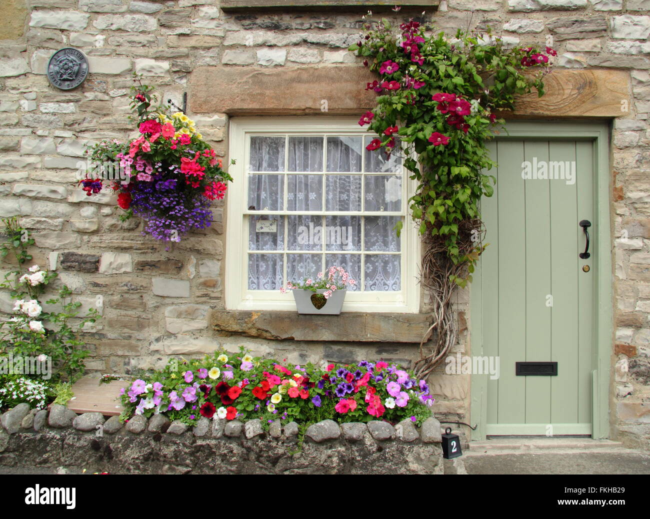 Summer flowers grow around the entrance to a traditional stone cottage in the Peak District National Park, Derbyshire UK Stock Photo