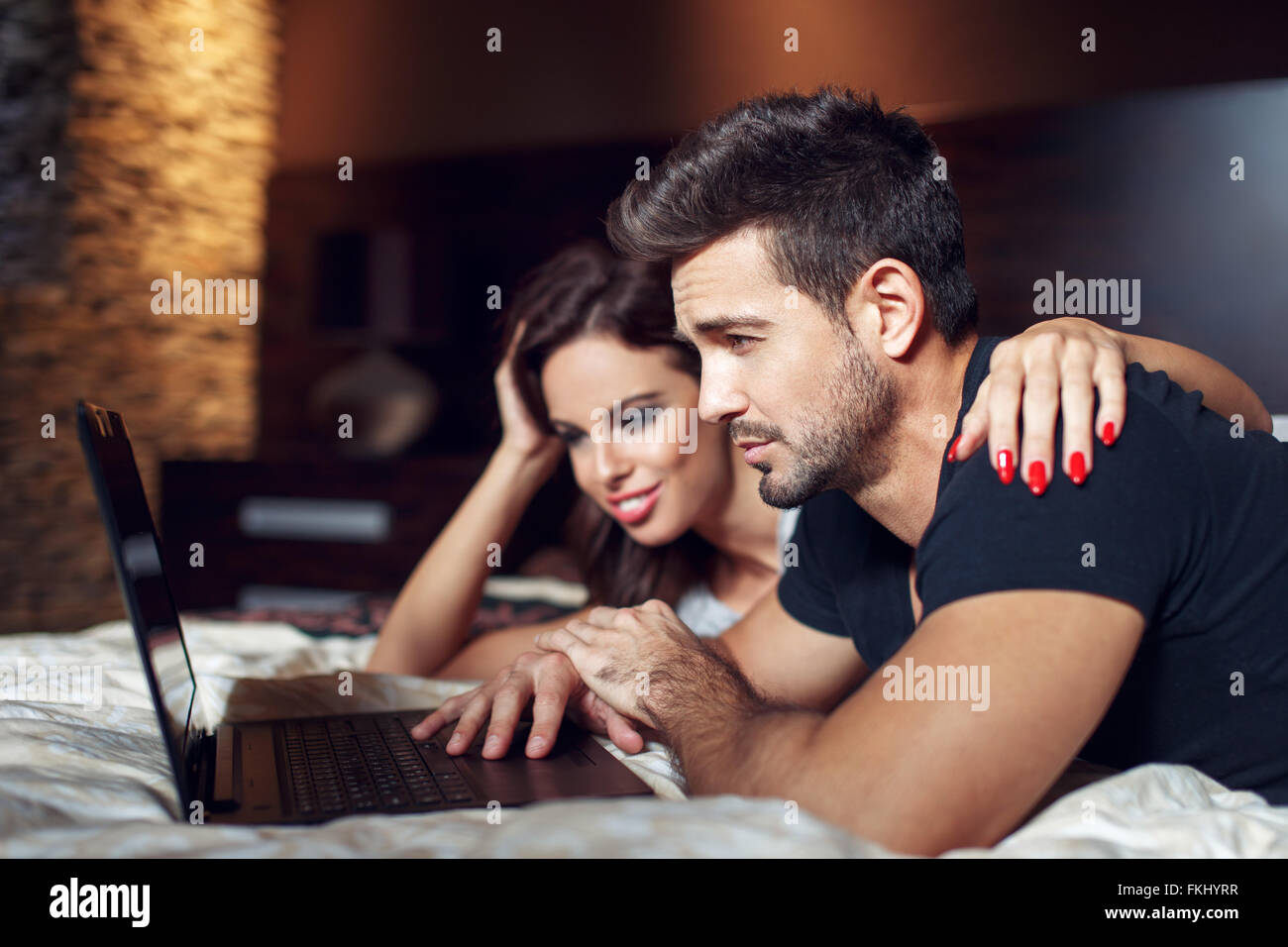 Couple prone on bed with laptop, casual man and woman online shopping. Worry about price Stock Photo