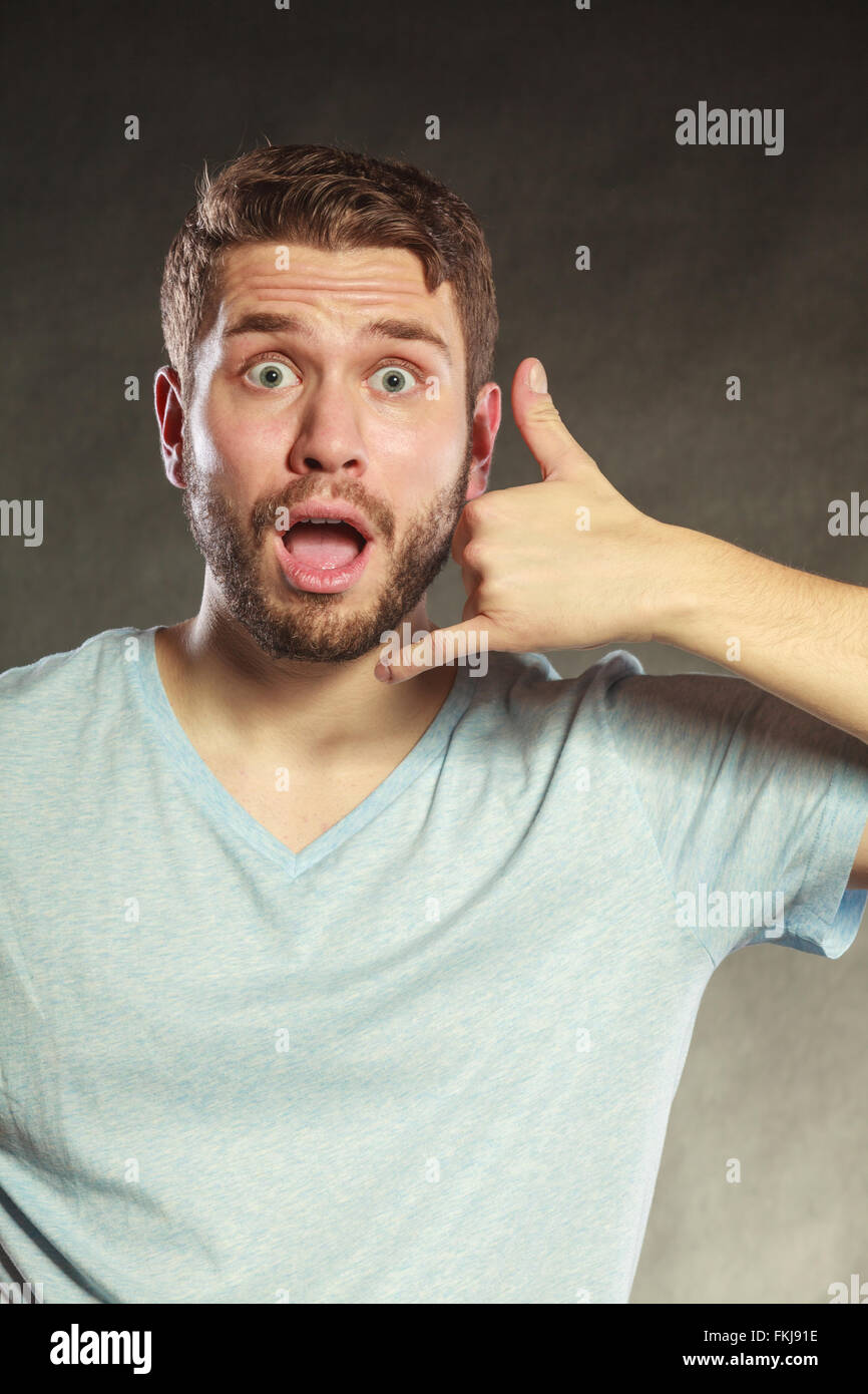 Surprised amazed young man guy with hand palm to ear showing call me gesture in studio on black. Stock Photo