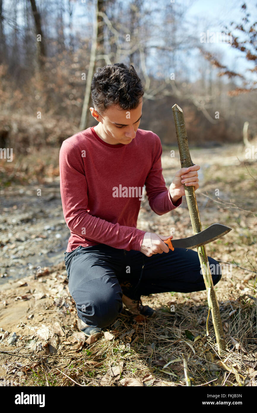 Teenage boy in the forest making a tool using a machete Stock Photo - Alamy