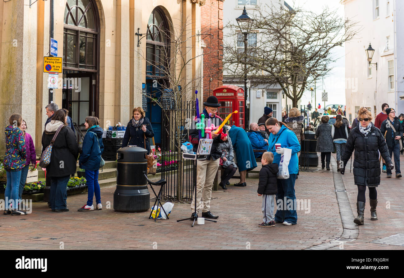 A street balloon seller makes animal shapes from balloons for a child  in Sidmouth town centre. Stock Photo