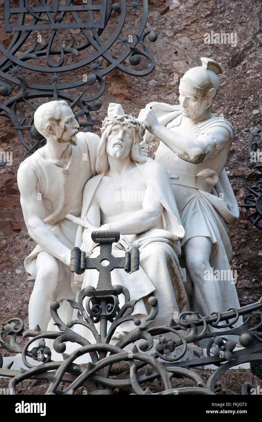white statue of christ with crown of thorns, roman soldier,one other figure and ironwork with cross santa cova walk  montserrat Stock Photo