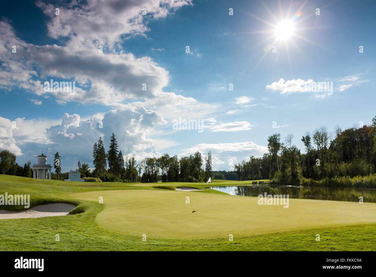 The sun shining over a golf course lined with buildings and trees Stock Photo